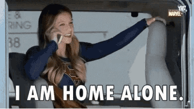 a woman is sitting in the back seat of a car talking on a cell phone and saying i am home alone .