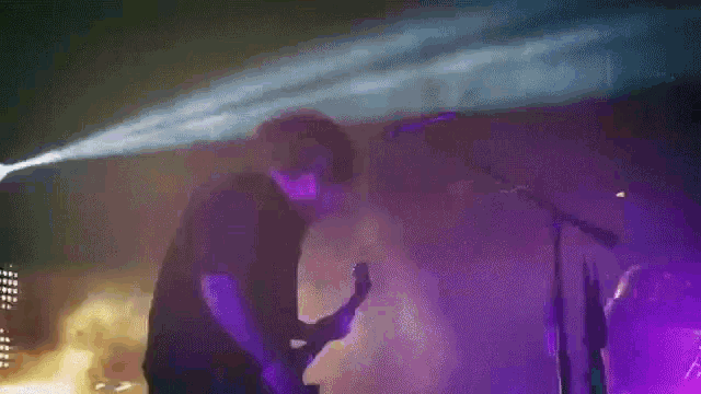 a man playing a guitar in front of a microphone in a dark room