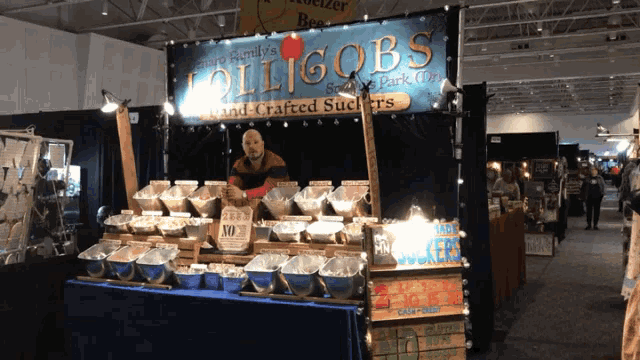 a man stands behind a booth selling lollipops