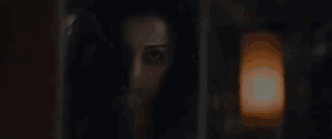 a woman is peeking out from behind a door and looking at the camera .