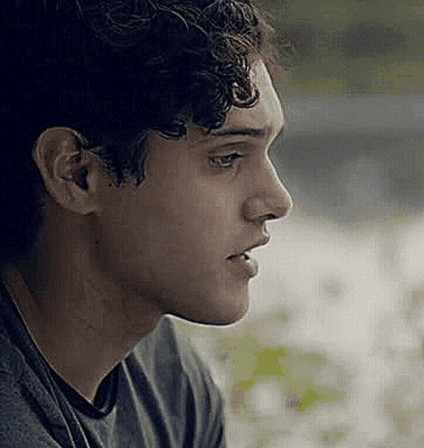 a close up of a young man 's face with curly hair looking away from the camera .