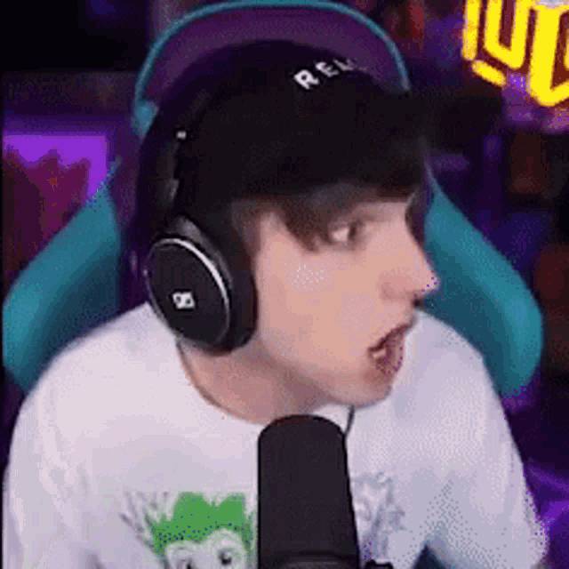 a man wearing headphones and a hat is talking into a microphone while sitting in a chair .