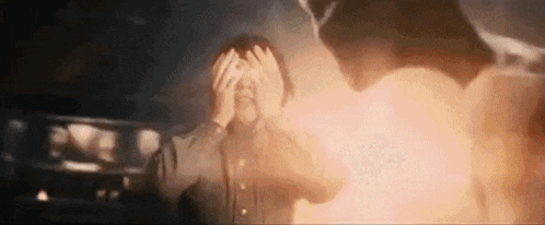 a man is covering his face with his hands while a fireball is coming out of his head .