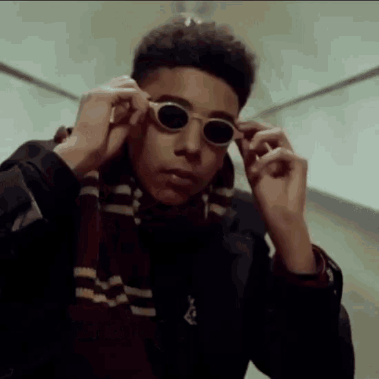 a young man wearing a scarf and sunglasses adjusts his glasses