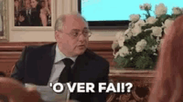 a man in a suit and tie is sitting at a table and talking to another man .