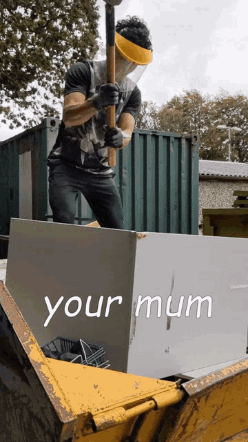 a man wearing a face shield holds a hammer over a dumpster that says your mum on it