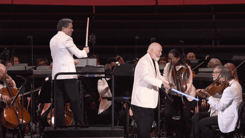 a man in a white suit holds a light saber in front of an orchestra