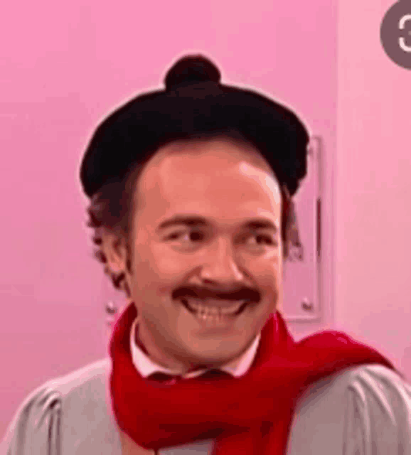 a man with a mustache wearing a black hat and a red scarf is smiling .