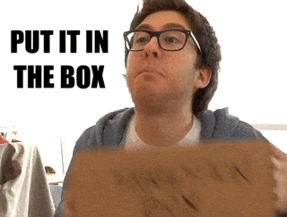 a man wearing glasses is holding a cardboard box with the words put it in the box behind him