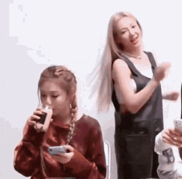 a woman is drinking a glass of milk while another woman looks at her cell phone .