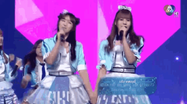 a group of girls singing into microphones on a stage with a sign that says ' a ' on it