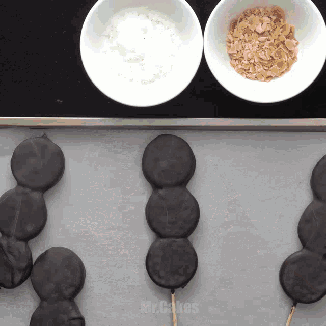 a tray of chocolate covered treats next to a bowl of powdered sugar and a bowl of toffee