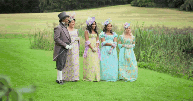 a man in a top hat is standing next to three women in fancy dresses