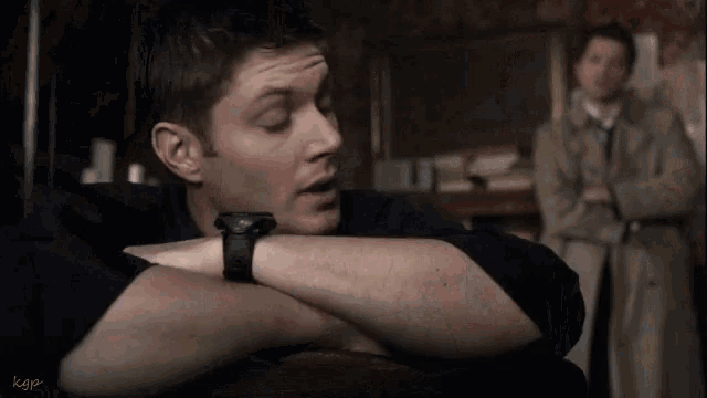 a man wearing a watch looks surprised while another man stands behind him