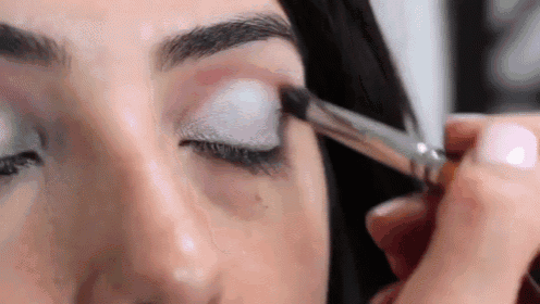 a woman is applying eye shadow with a brush to her eye .