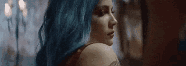 a woman with blue hair is looking over her shoulder at the camera .