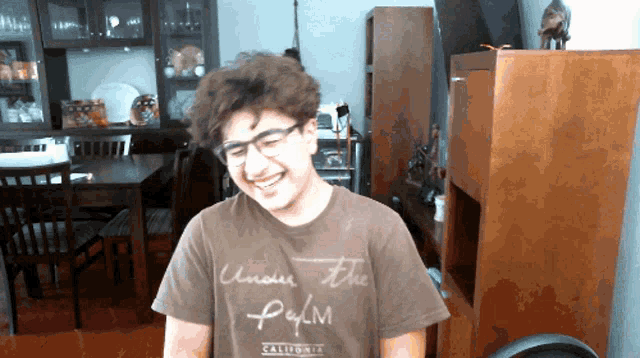 a young man wearing glasses and a brown shirt that says under the palm