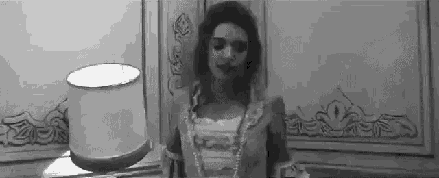 a woman in a dress is standing next to a lamp in a room .