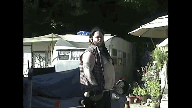 a man in a plaid shirt is holding a skateboard in front of a trailer