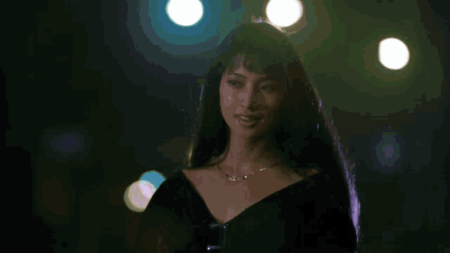 a woman in a black dress is standing in a dark room with lights behind her