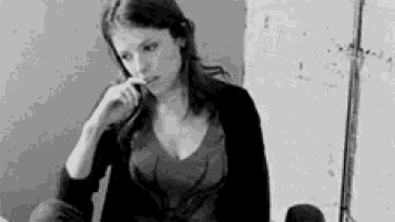 a black and white photo of a woman smoking a cigarette while sitting on a chair .