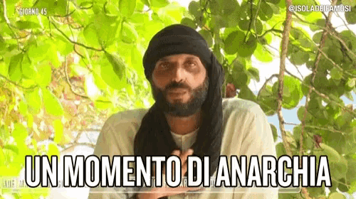a man with a beard and a scarf around his head is standing in front of a tree and says un momento di anarchia