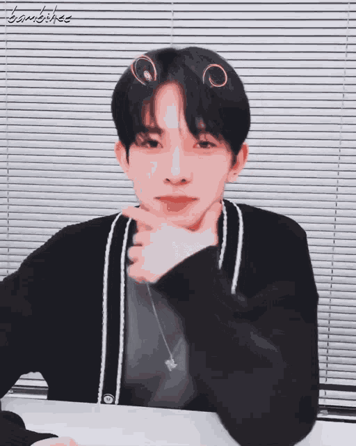 a young man sitting in front of a window with blinds has a sticker on his head that says ' bambihee '
