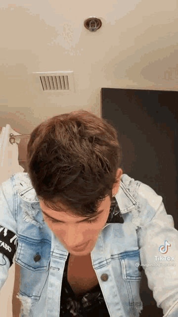 a young man in a denim jacket is standing in a bathroom looking down .