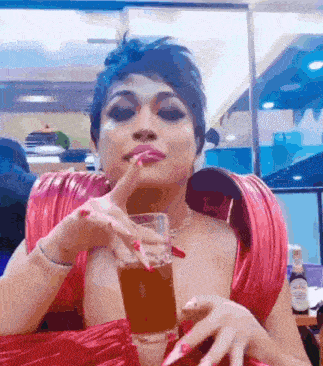 a woman in a red dress is drinking from a glass through a straw .
