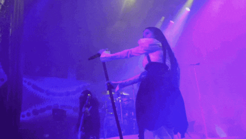 a woman singing into a microphone on a stage with purple lights behind her .