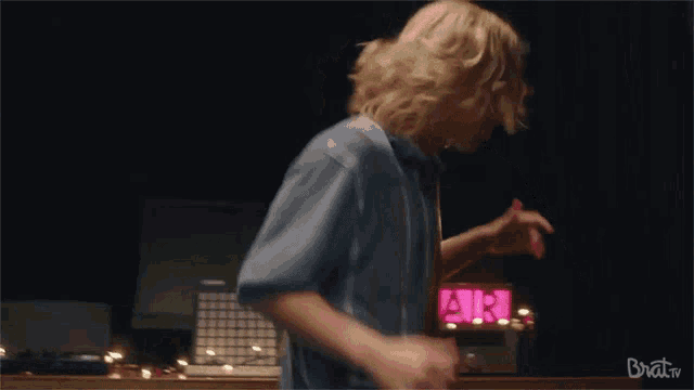a man in a blue striped shirt is dancing in front of a sign that says brat tv