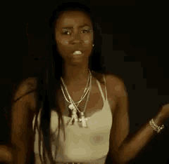 a woman in a white tank top and necklace is standing in front of a black background .