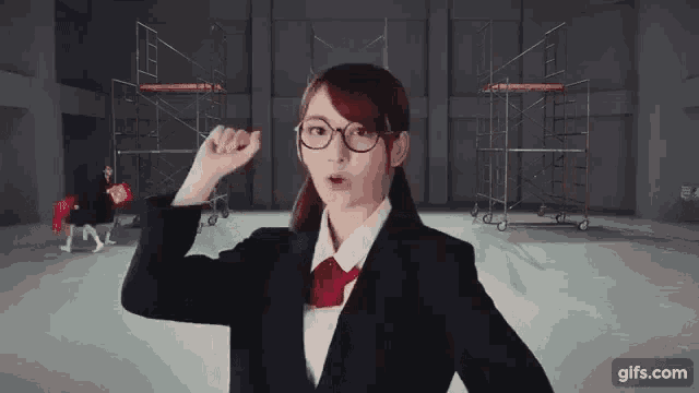 a woman wearing glasses and a suit is standing in a room with scaffolding in the background .