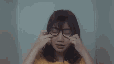 a woman wearing glasses and a yellow shirt is crying .