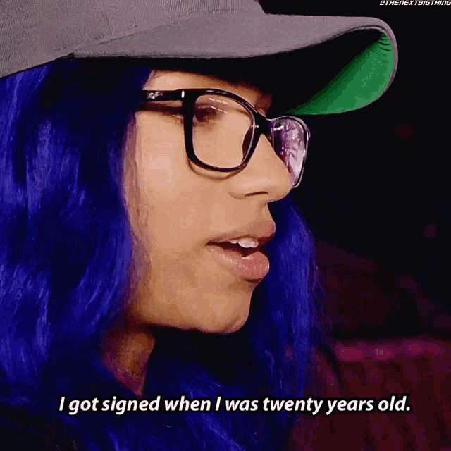 a woman with blue hair is wearing glasses and a hat and says i got signed when i was twenty years old