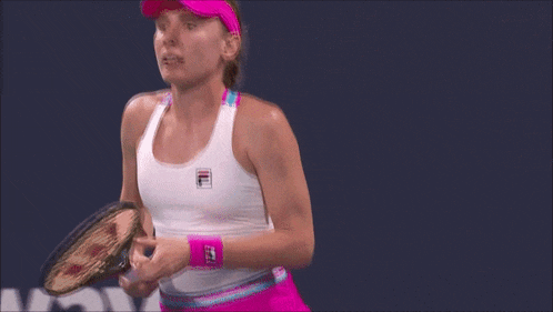 a woman holding a tennis racquet wearing a white tank top with a fila logo on it