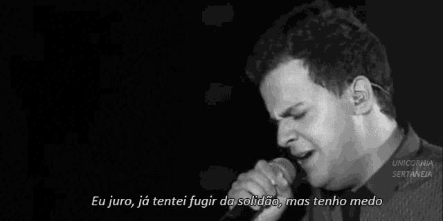 a black and white photo of a man singing into a microphone with a caption .
