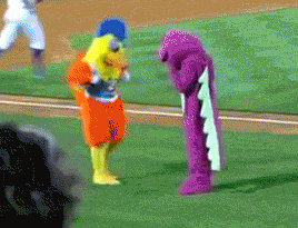 two mascots are standing on a baseball field one is a yellow duck and the other is a purple shark