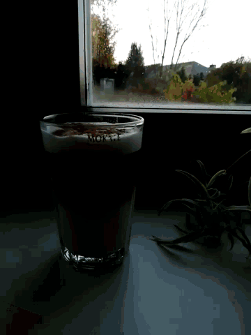 a glass with the word moka on it sits next to a window