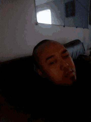 a man with a shaved head is laying down in a dark room