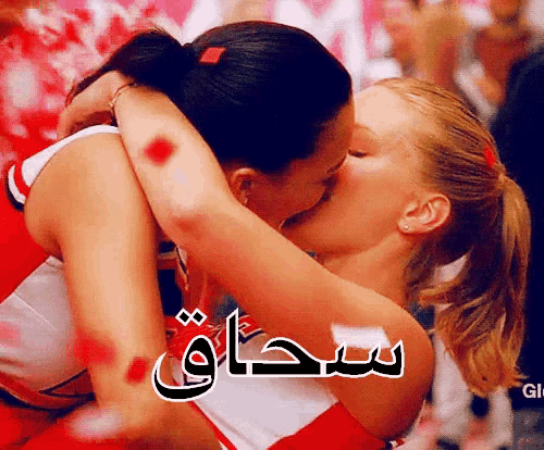 two cheerleaders kissing in front of a crowd with arabic writing on the bottom