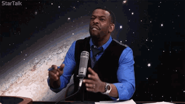 a man in a blue shirt and black vest is talking into a microphone with the words startalk above him
