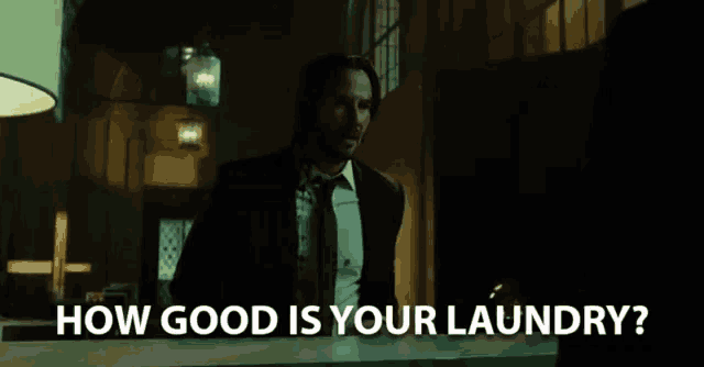 a man in a suit and tie is standing in front of a counter asking how good is your laundry .