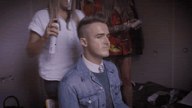 a man in a denim jacket is getting his hair blow dried by a woman