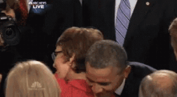 a man in a suit and tie kisses a woman in a crowd with anchors live on the screen behind him