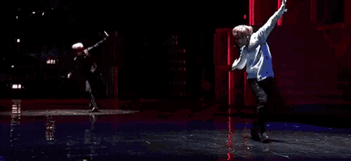 a couple of dancers are performing on a stage in front of a red wall .