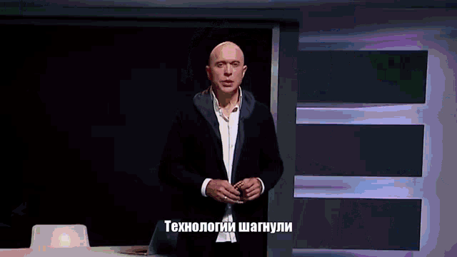a bald man in a suit stands in front of a screen that says " технологии "