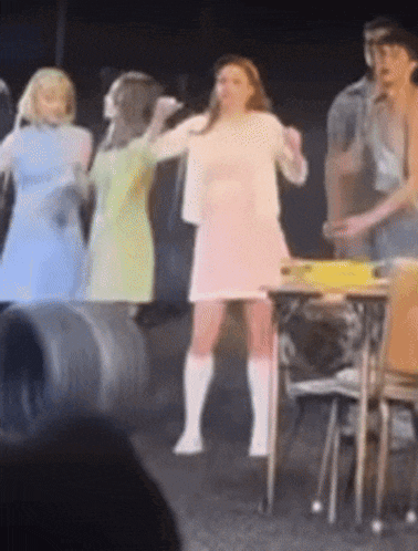 a woman in a pink dress is standing on a stage with other people