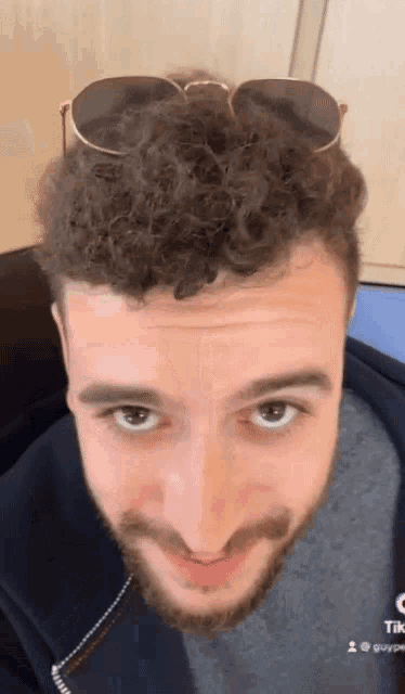 a man with curly hair wearing sunglasses and a beard looks at the camera