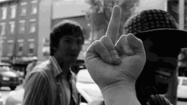 a man in a hat is giving the middle finger to another man in a black and white photo .